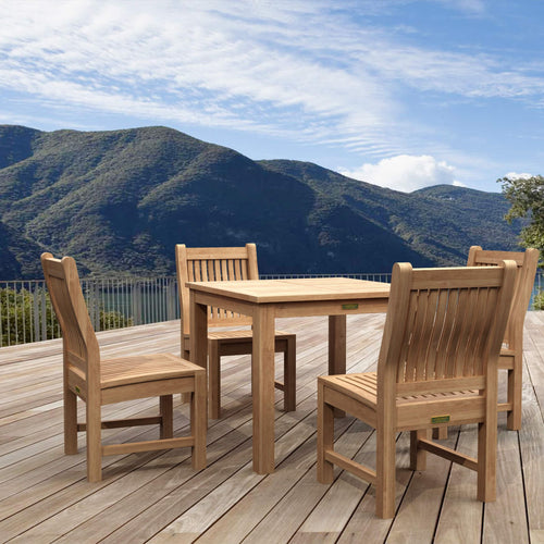 A 4-piece outdoor dining set made of natural teak wood, including a rectangular table and four matching slatted chairs, arranged on a wooden deck with a scenic mountain backdrop.