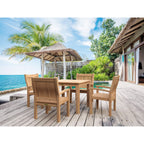 A wooden outdoor dining set with a rectangular table and four matching armchairs placed on a light deck beside a pool, with palm trees, ocean water, and a thatched umbrella in the background.