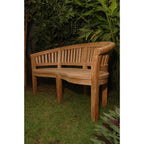 A curved wooden garden bench with a slatted backrest, shown outdoors on grass with leafy plants in the background.