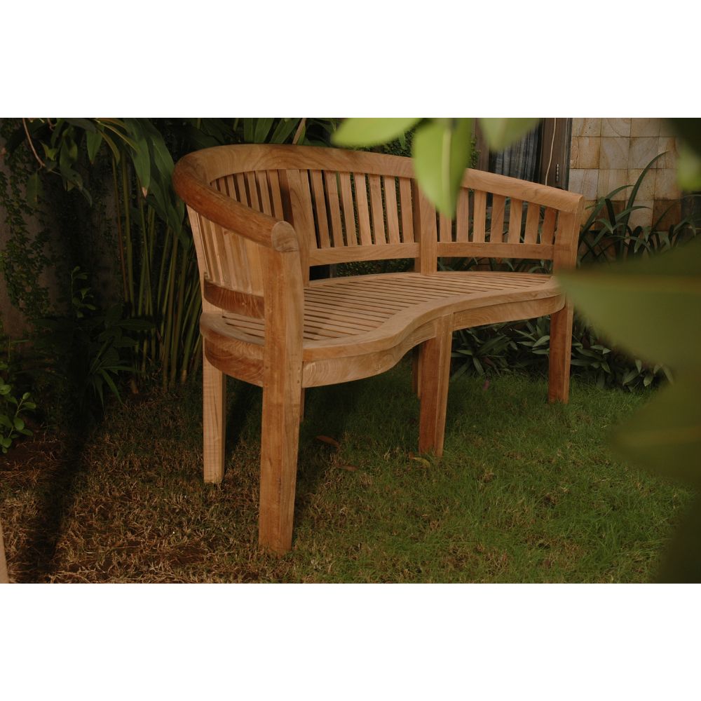 A curved wooden garden bench with a slatted back and seat, placed on grass in an outdoor garden setting with plants and a stone wall in the background.