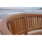 Close-up of a curved wooden outdoor bench with vertical slats, shown against a blurred beach and ocean background.