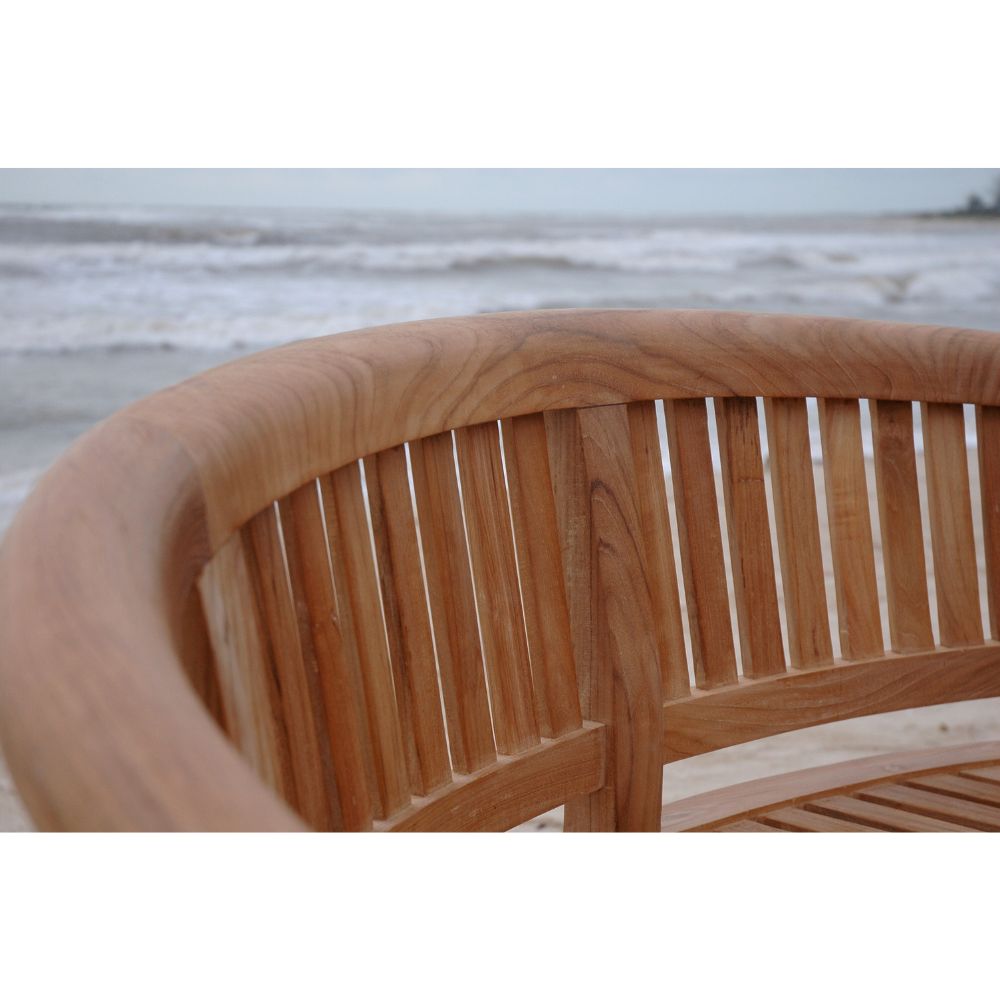 Close-up of a curved wooden outdoor bench with vertical slats, shown against a blurred beach and ocean background.