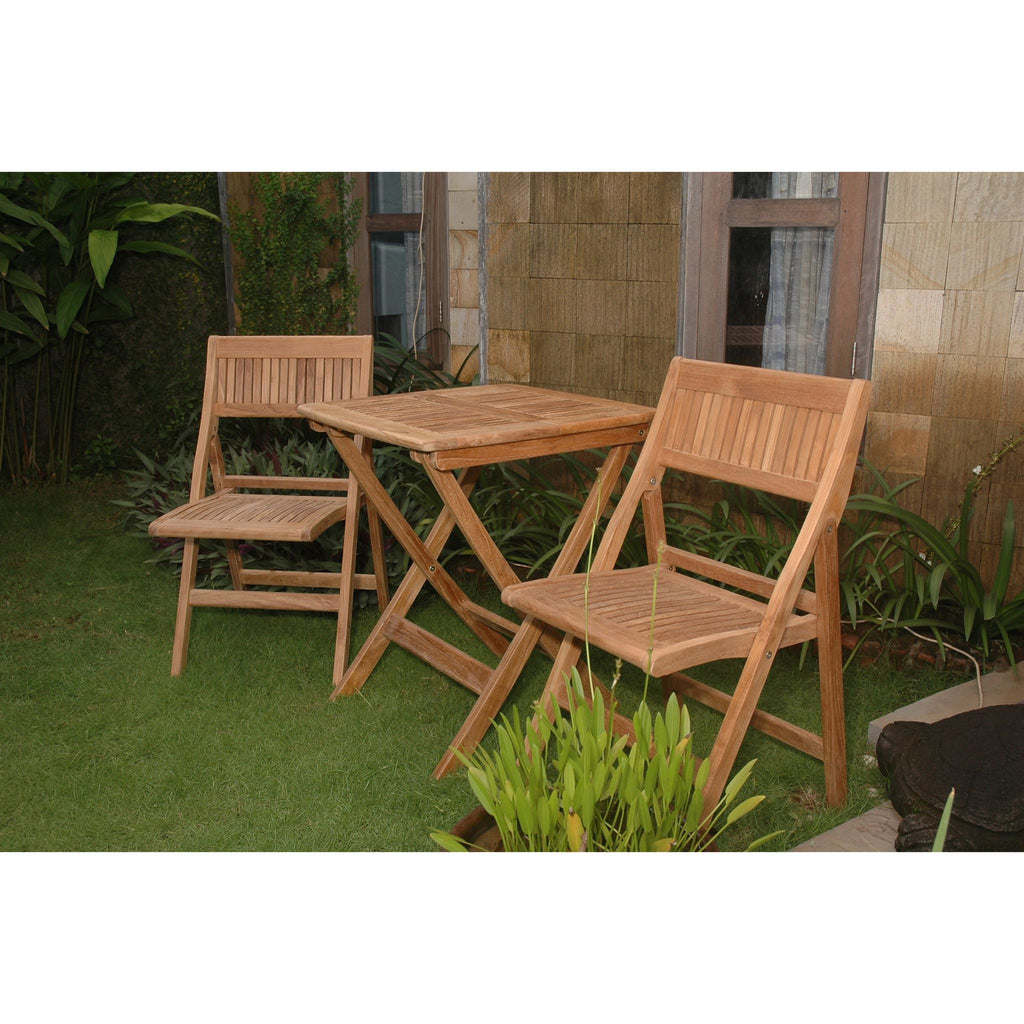 A three-piece outdoor wooden bistro set consisting of a square folding table and two matching folding chairs, placed on a green lawn in front of a stone wall.