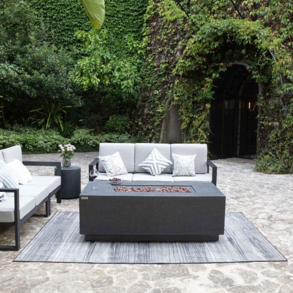 Outdoor patio set with gray cushions and a fire pit table in a garden setting.