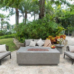 Outdoor patio with a fire pit table, chairs, and decorative elements in a garden setting.