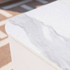Close-up of a white marble-patterned tabletop corner with a smooth white base, photographed indoors on a patterned rug.
