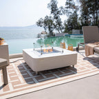 Outdoor patio with fire pit table, chairs, and view of water and trees
