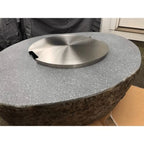 A round stainless steel fire pit insert with a brushed metallic finish, set into a textured gray stone base.