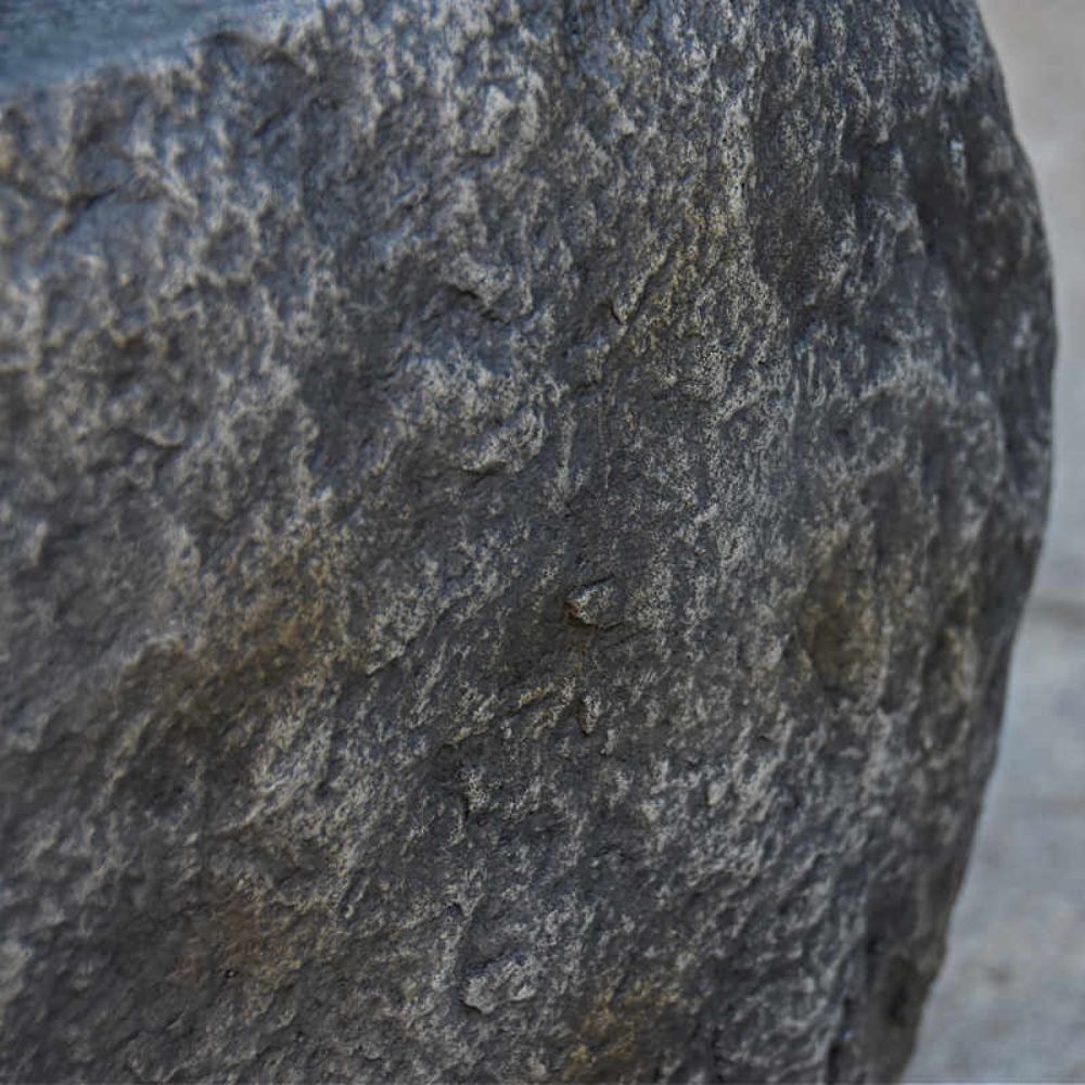 A close-up of a rough, textured dark gray stone or concrete surface with natural speckling and tonal variation.