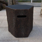 A rustic hexagonal stone stool with a dark textured surface and a rectangular cutout handle, set on a light gray tiled patio.