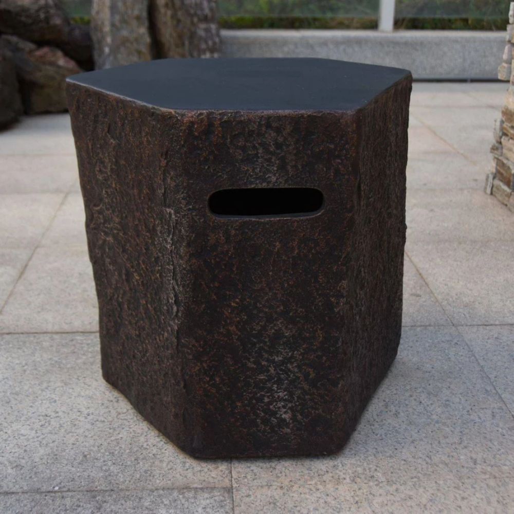 A rustic hexagonal stone stool with a dark textured surface and a rectangular cutout handle, set on a light gray tiled patio.