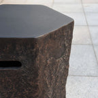 A close-up of a dark, rustic hexagonal stone or concrete bin with a textured surface and a slot cutout on the side, set against a light gray tiled background.