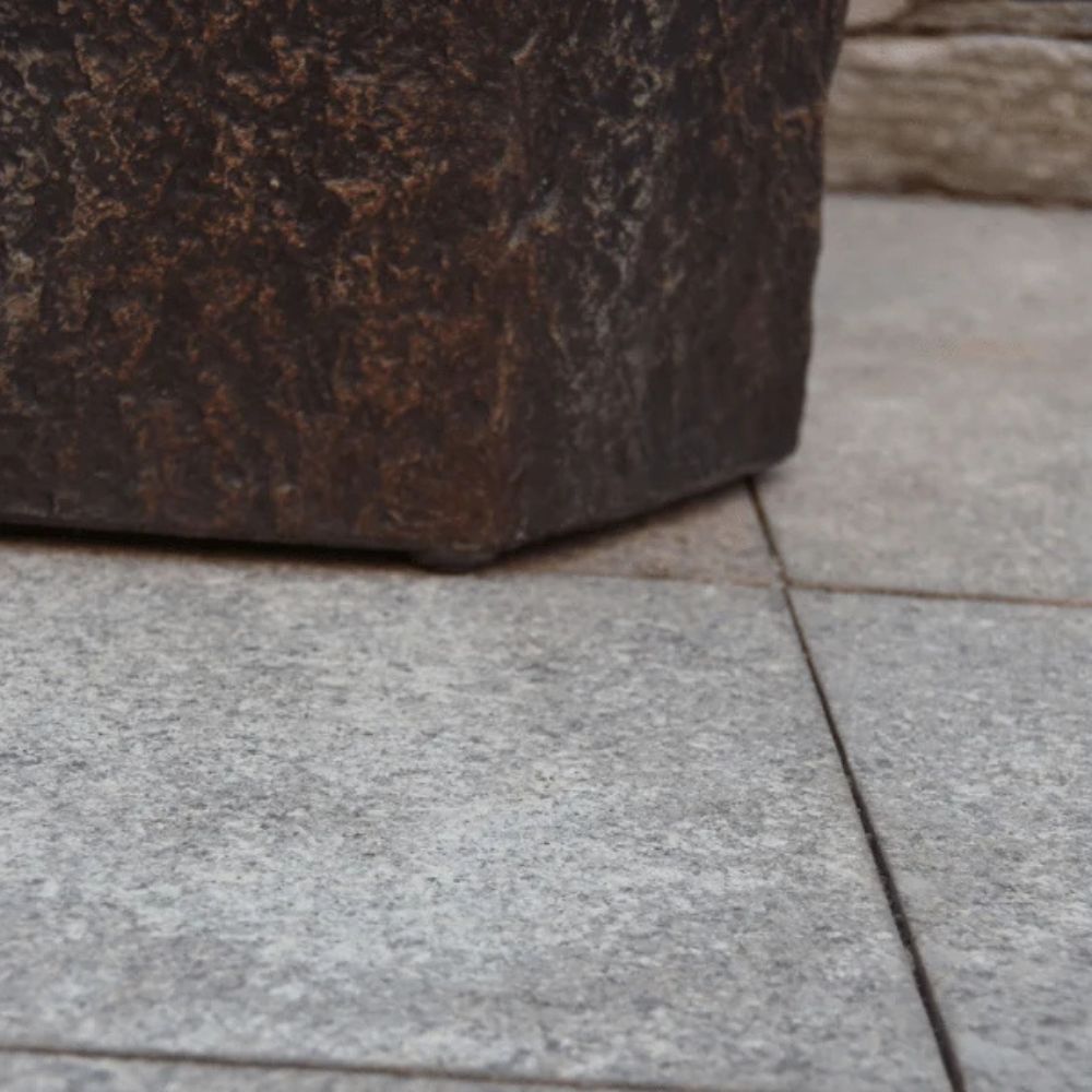 Close-up of a dark brown textured stone planter corner resting on light gray stone pavers.