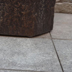 Close-up of a dark brown textured stone planter corner resting on light gray stone pavers.