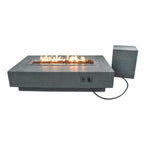A rectangular outdoor fire pit table with a modern concrete-look finish, shown lit with orange flames. A matching square side component and power cord are visible against a plain white background.