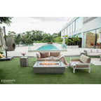Outdoor patio with fire pit table, chairs, and a pool in the background.