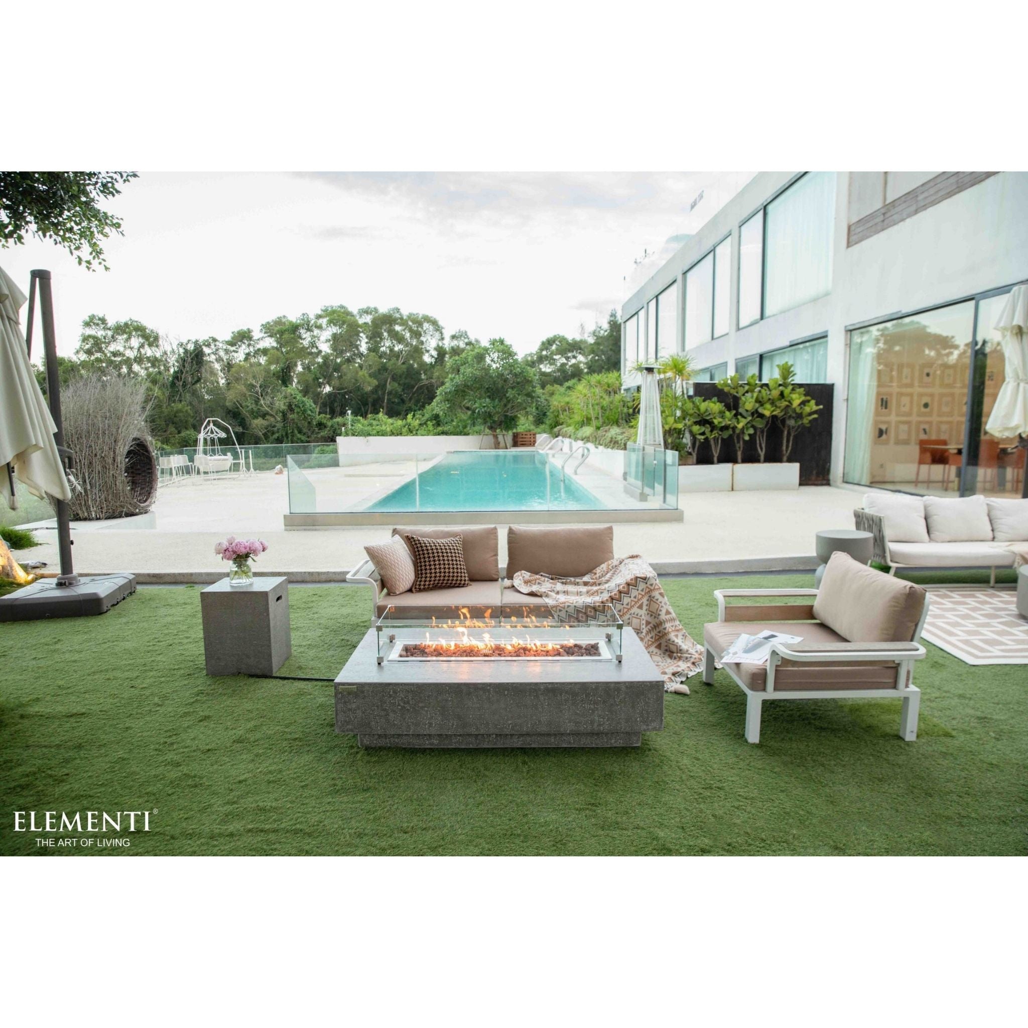 Outdoor patio with fire pit table, chairs, and a pool in the background.