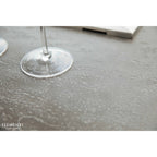 A close-up of a gray stone or concrete tabletop with water droplets, featuring the base of a clear wine glass and a partial object in the background. The brand name ELEMENT1 is visible in the bottom-left corner.