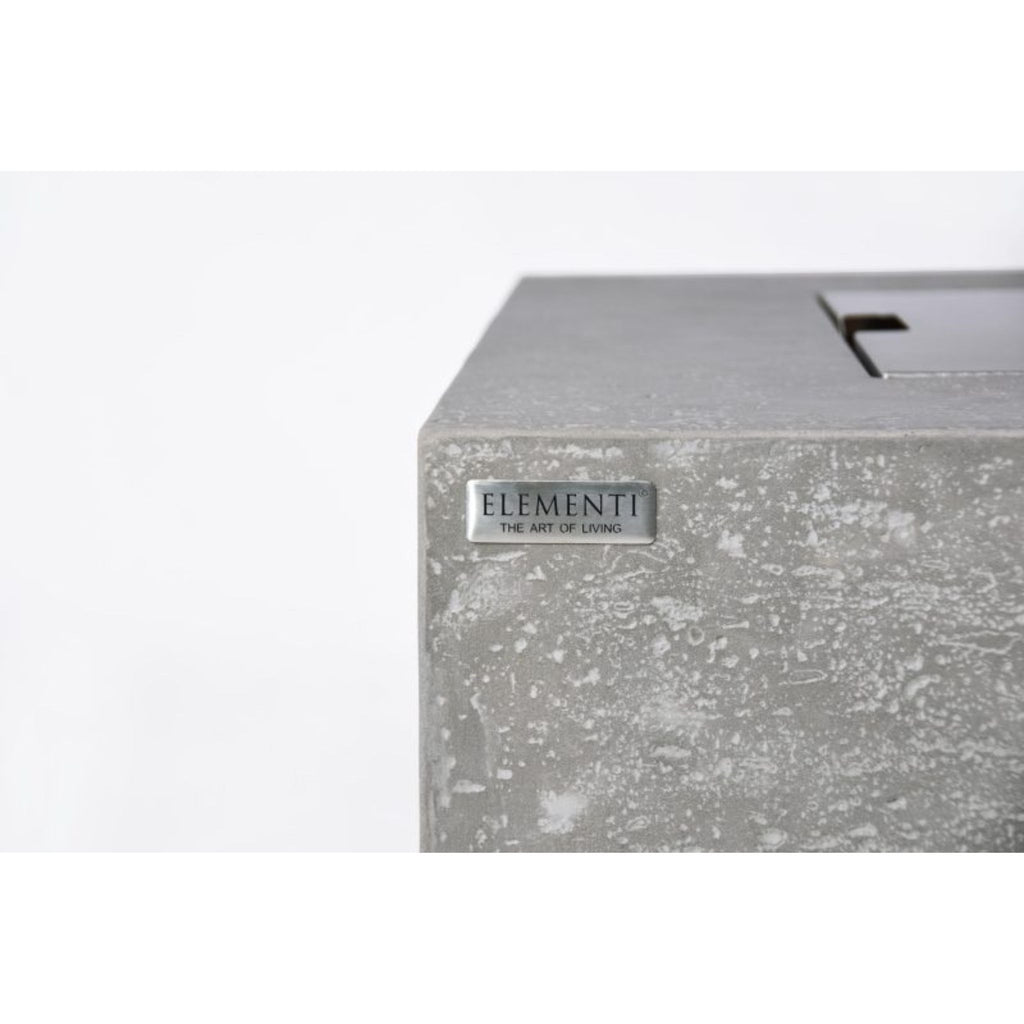 Close-up of a textured gray concrete or stone-look rectangular product corner with a small silver plaque reading ELEMENTI THE ART OF LIVING.