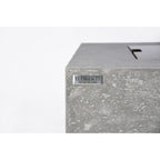 Close-up of a textured gray concrete or stone-look rectangular product corner with a small silver plaque reading ELEMENTI THE ART OF LIVING.