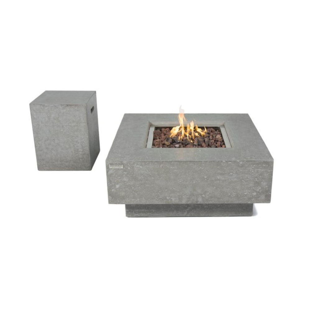 A square concrete fire pit table with a visible flame and dark stones inside, shown alongside a matching square side pedestal on a plain white background.