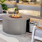 A round concrete fire pit table with a visible flame and fire rocks, shown in a modern living room setting next to a white chair and a propane tank.