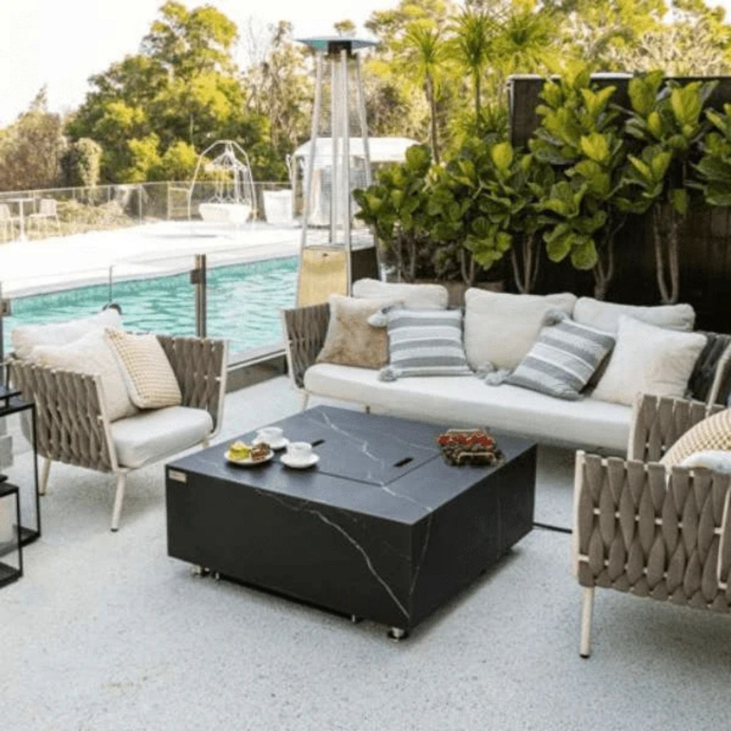 Outdoor patio setup with fire pit table, chairs, and a pool in the background.