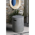 A cylindrical concrete storage bin or planter in a gray finish, featuring a cutout handle on the side, set outdoors against a stone wall with a potted plant behind it.