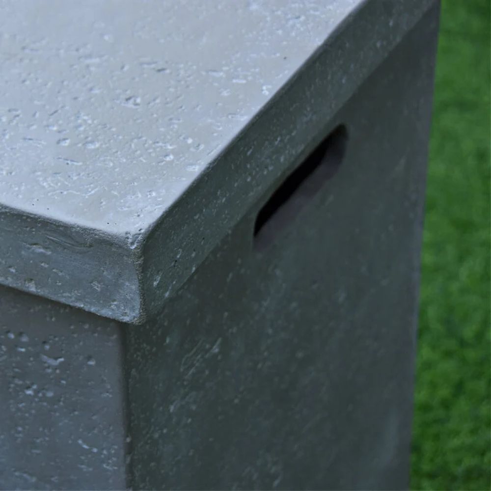 Close-up of a gray concrete or stone planter box with a textured surface and a side cutout, shown outdoors next to green grass.