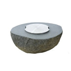 A round stone fire pit with a textured dark gray stone base and a smooth, flat gray top featuring a small silver metal wind guard, shown on a plain white background.