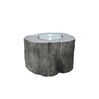 A round, log-shaped fire pit table with a textured gray bark-like finish and a clear glass wind guard on top, shown against a plain white background.