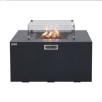 A black outdoor fire pit table with a clear glass wind guard and active flames, shown against a plain white background.