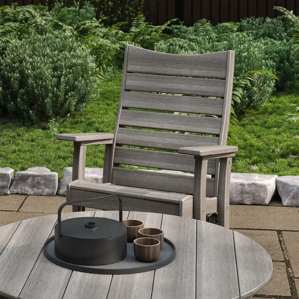 Gray wooden chair on a patio with a small round table and items on a sunny day.