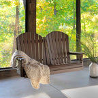 Wooden porch swing with a blanket on a porch with a view of trees.