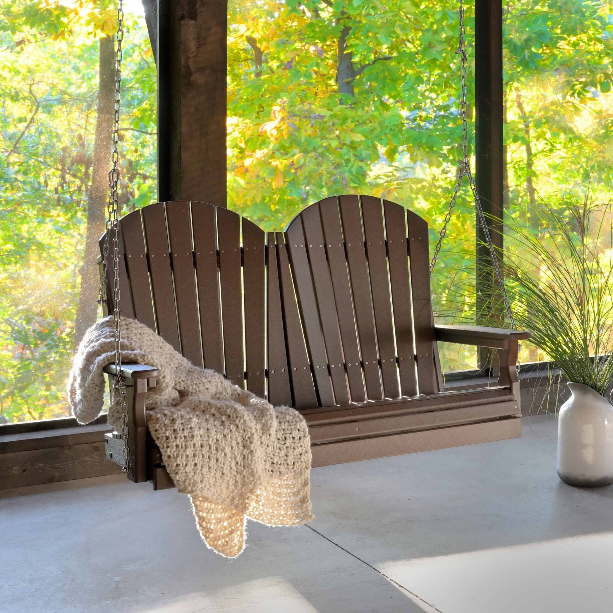 Wooden porch swing with a blanket on a porch with a view of trees.
