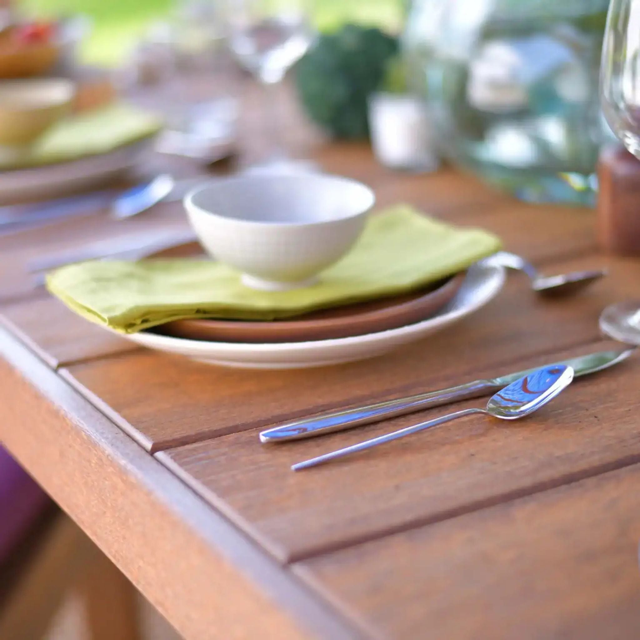 Dining table setup with plates, bowls, and cutlery on a wooden surface.