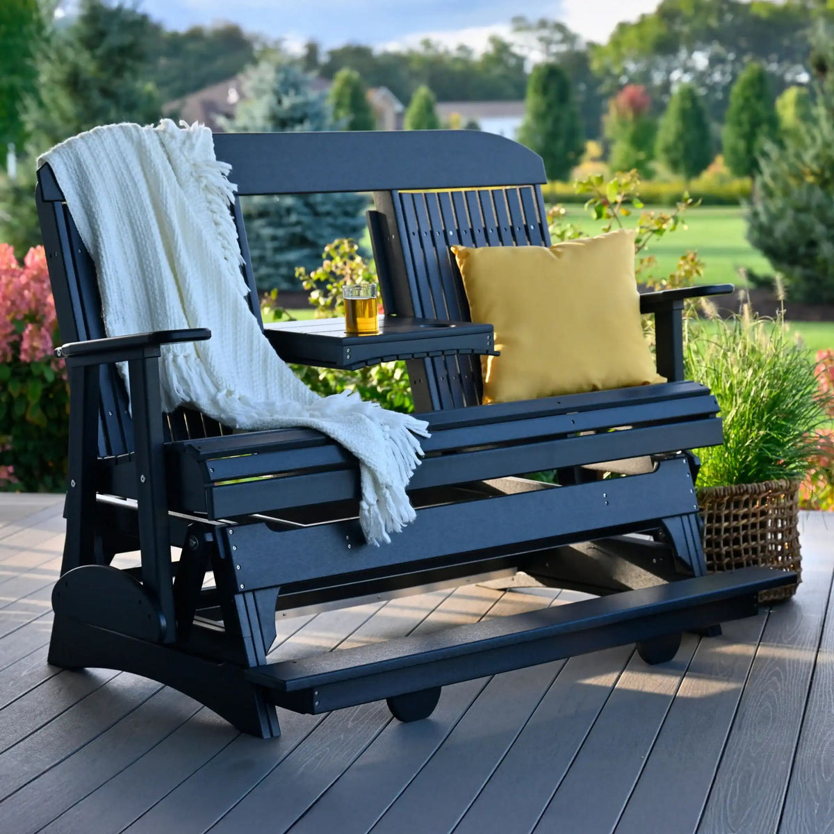 Blue outdoor swing chair with a white blanket and yellow pillow on a wooden deck.