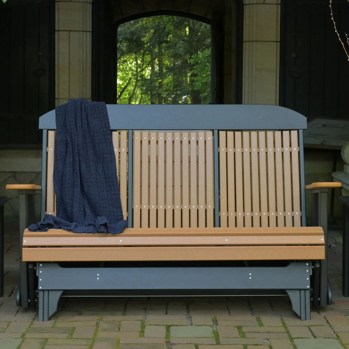 A wooden outdoor bench with a dark blue-gray frame and light natural wood slats, shown in a covered patio setting with a dark blue throw blanket draped over the left side.