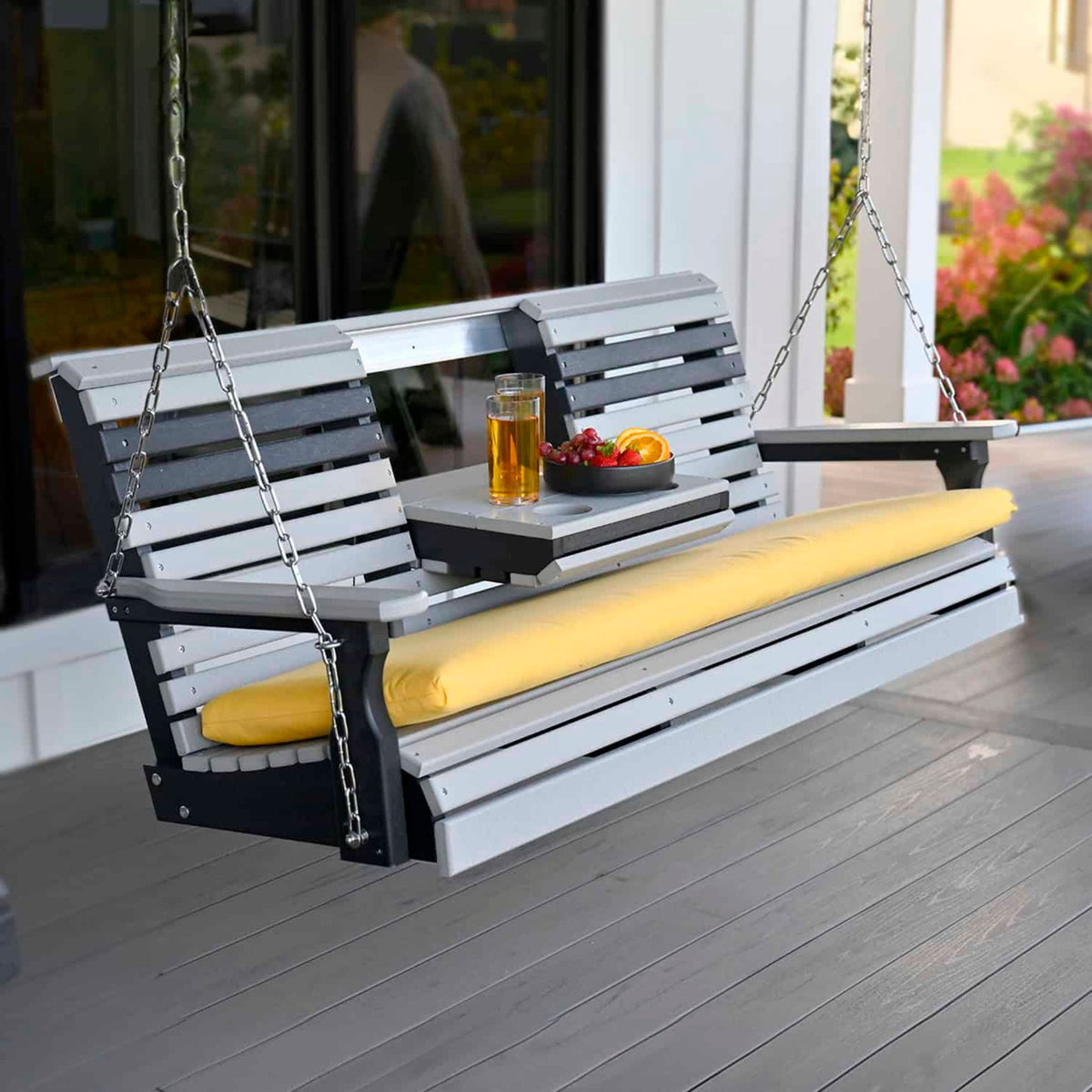 Wooden porch swing with yellow cushion on a deck, featuring a drink and fruit bowl.