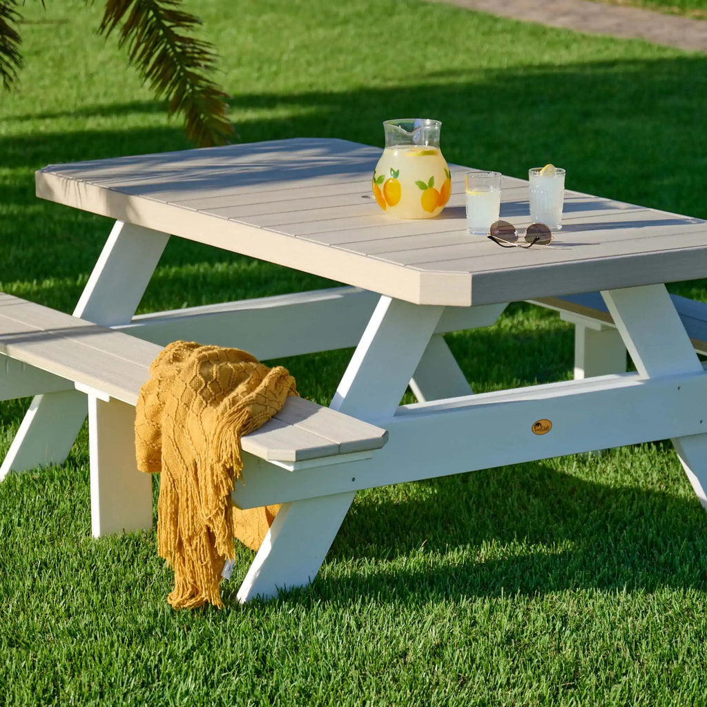 White picnic table with a yellow blanket on a grassy area