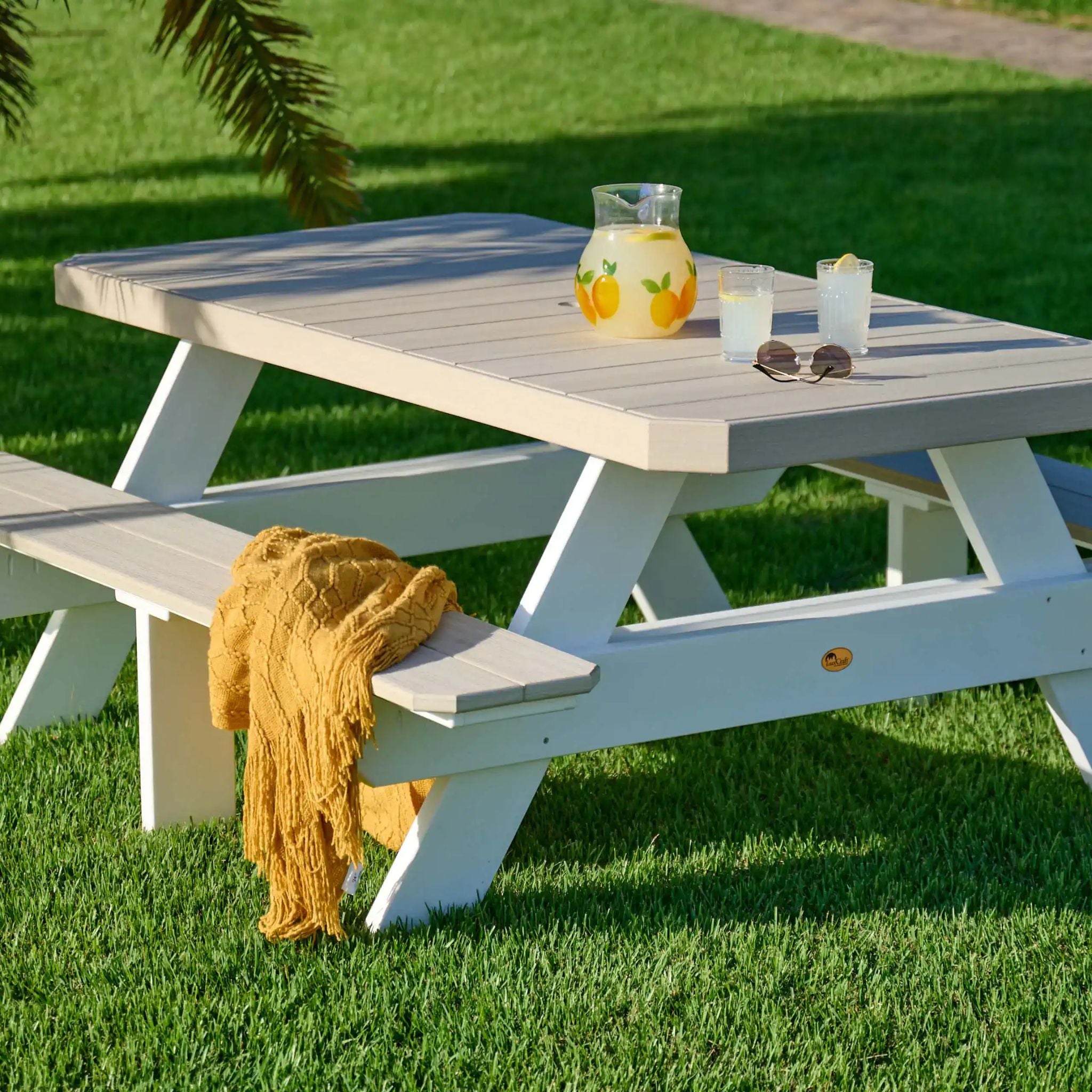 White picnic table with a yellow blanket on a grassy area