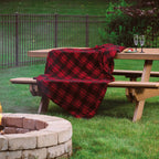 Red plaid blanket draped over a wooden picnic table with a fire pit in the foreground.