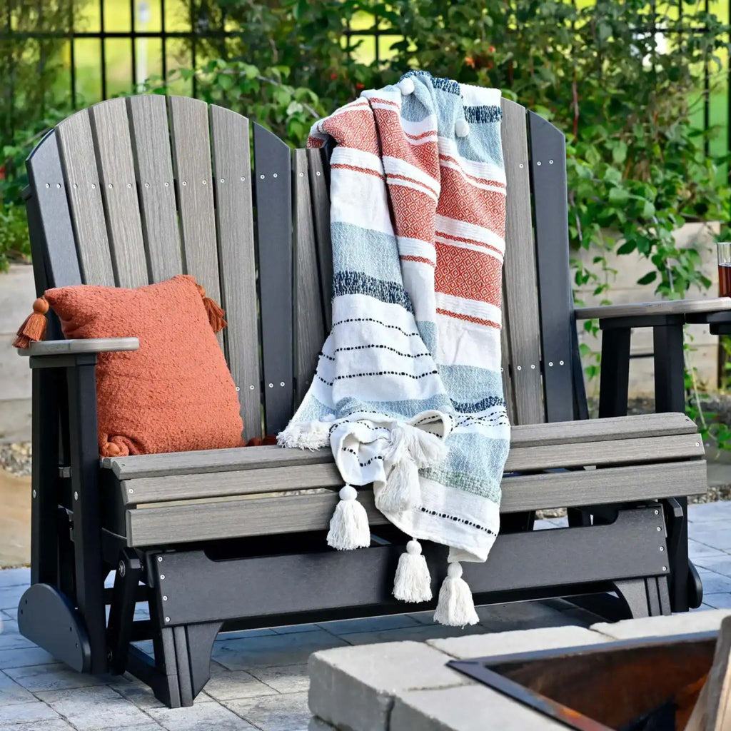 Gray Adirondack chair with a striped blanket and orange pillow on a patio.