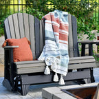 Gray Adirondack chair with a striped blanket and orange pillow on a patio.
