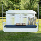 White wooden swing with blue cushion and striped pillow on a grassy area with trees in the background