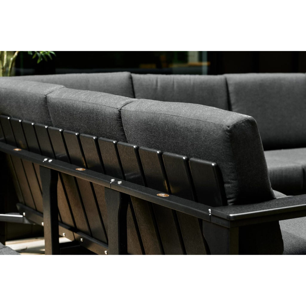 Close-up of a dark gray outdoor sectional sofa with thick cushioned backrests and a black slatted frame, shown against a dark background.