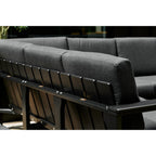 Close-up of a dark gray outdoor sectional sofa with thick cushioned backrests and a black slatted frame, shown against a dark background.
