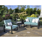Outdoor patio furniture set including a two-seat sofa, a matching armchair, and a small round side table on a stone patio with a landscaped garden background.