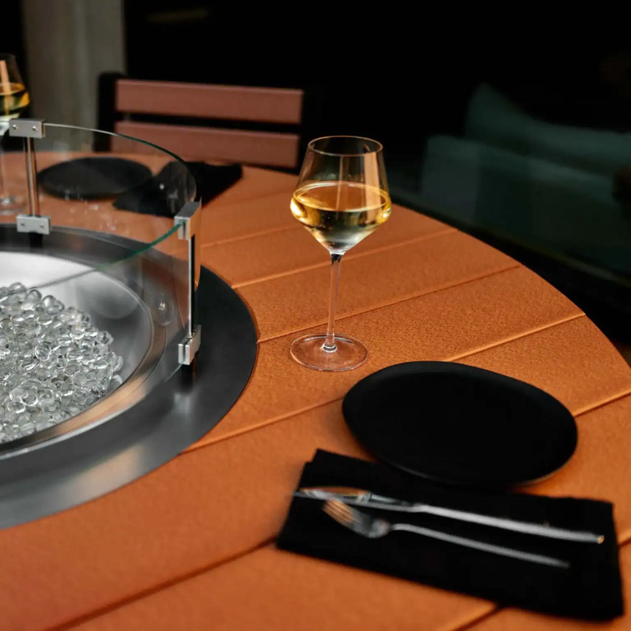 Glass bowl with decorative stones on a round table with a glass of wine and black plate.