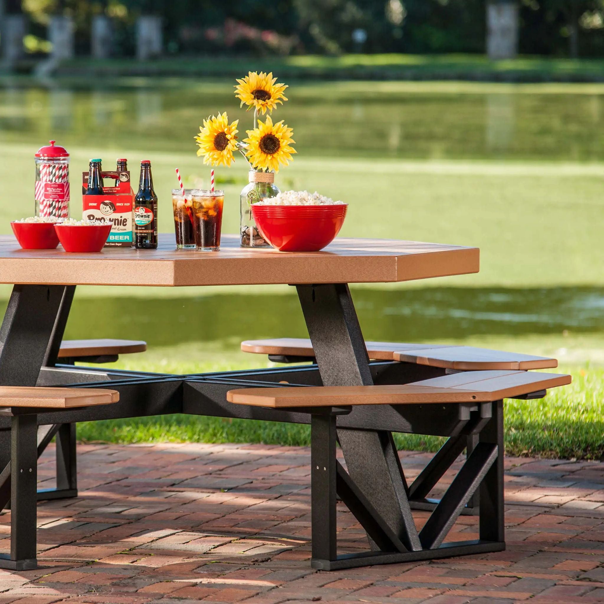 Outdoor picnic table with drinks, snacks, and flowers by a lake.